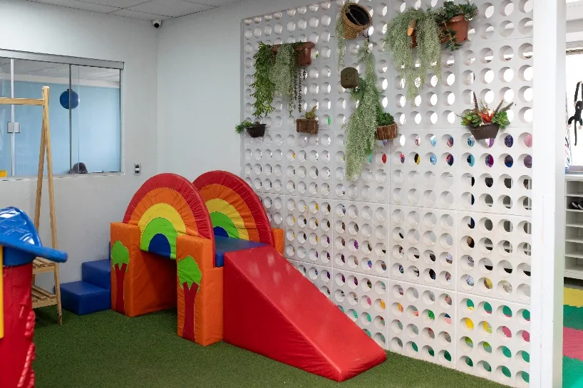 Espaço de recreação com escorregador em formato de arco-íris e parede vazada com plantas